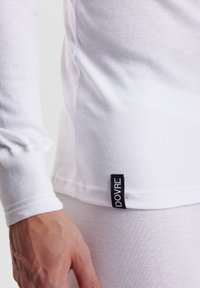 Langermet hvit t-skjorte laget av bomull, med en tettsittende design og en svart etikett med "DOVRE" på kanten.