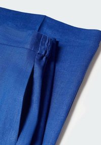 Jasnoniebieska złożona tkanina z widocznymi szwami i detalami fałd na jasnoszarym tle.