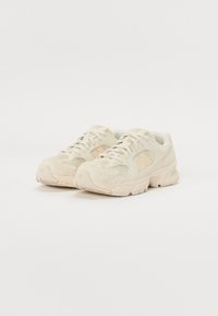 Scarpe sportive beige con tomaia in rete e dettagli sintetici, dotate di suola in gomma arrotondata e motivi testurizzati a contrasto. Lacci davanti.