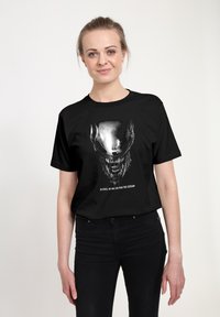 Černé bavlněné tričko s potiskem tváře tvora, metalickým leskem a bílým textem: „VE VESMÍRU NIKDO NESLYŠÍ TVŮJ KŘIK.“