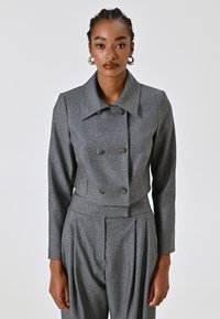 Veste cropped métallique grise avec un col cranté, fermeture double boutonnage et accents de boutons floraux, associée à un pantalon taille haute.
