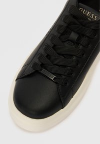 Černé kožené tenisky s kulatou špičkou, texturovanými černými tkaničkami a bílou gumovou podrážkou; mají malé logo na boku.