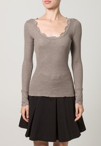 Rebrasti top dugih rukava u tofi boji s valovitim izrezom i čipkom na rukavima; uparen s crnom suknjom na zvono.