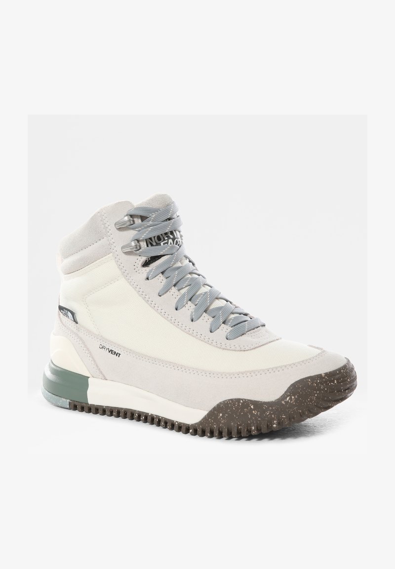 Botte de randonnée montante beige et blanc cassé avec des lacets gris, semelle texturée marron foncé et marquage sur le côté et sur la languette.