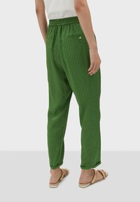 Green patterned pants with an elastic waistband, tapered shape, and two pockets, featuring a small gold accent on the back.