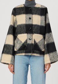 Cekowany wełniany żakiet w czerni i kremie o pudełkowym kształcie, okrągłym dekolcie, z guzikami z przodu i dwoma naszytymi kieszeniami.