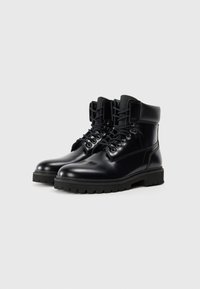 Bottines en cuir noir avec une finition lisse, bout rond et semelle épaisse en caoutchouc avec des semelles à motifs. Conçues avec des œillets en métal et des lacets.