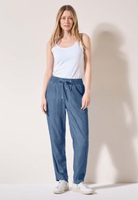 Pantaloni azzurri chiari, dalla vestibilità morbida, con vita regolabile tramite cordoncino, realizzati in un tessuto soffice. Abbinati a un top bianco senza maniche e sneakers bianche.