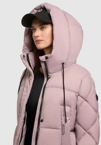 Svetloružový puffa kabát s veľkou kapucňou, prešívaným dizajnom, čiernymi zipsami a šnúrkami. Nosený cez čierny top, s čiernou čiapkou.