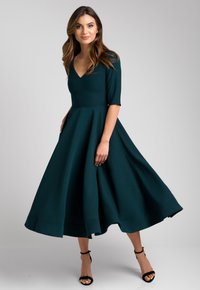Turkusowa midi sukienka z dopasowanym gorsetem, dekoltem w kształcie litery V i plisowanym dołem. Wykonana z gładkiego materiału, posiada półrękawy oraz rozkloszowany dół.