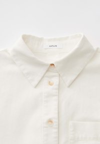 Witte overhemden met puntkraag, drie zichtbare beige knopen, een borstzak en een 'OPUS' merklabel aan de binnenkant van de kraag.