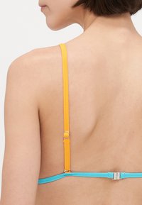 Twee riemen in helder geel en blauw vormen de achterkant van een beha, met slanke hardware en een eenvoudig, minimalistisch ontwerp.
