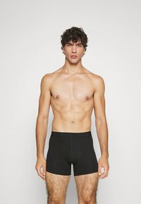 Melni bokseršorti no gludas auduma, ar ciešu piegulumu, vidēja augstuma garumu līdz augšstilbiem un vienkāršu dizainu bez redzamām rakstām vai logotipiem.