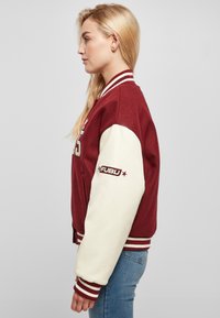 Red and cream varsity jacket with ribbed collar and cuffs, featuring a logo on the left sleeve and a wool body with leather sleeves.
