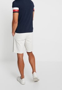 Camisa de manga corta en color navy con acentos en blanco y rojo, combinada con pantalones cortos blancos y zapatillas blancas, vista desde la parte de atrás.