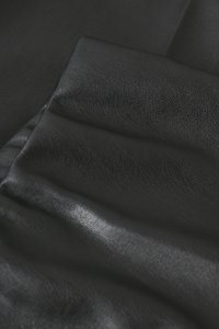 Mustast sünteetilisest nahast voltis kangas, kus on näha tekstuuri ja kerget läiget siledal, kortsus pinnal.