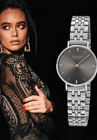 Montre en maille argentée avec un cadran rond noir texturé et des accents en or rose. Le bracelet comporte des maillons décoratifs et des embellissements en cristal.