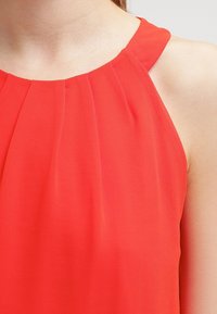 Blusa rossa senza maniche con texture plissée e scollo rotondo, realizzata in tessuto leggero, caratterizzata da una finitura liscia e priva di ulteriori decorazioni.