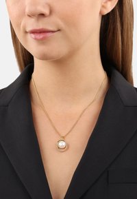Goldene Halskette mit einem runden Perlenanhänger und einem Ring aus klaren Steinen. Die Kette ist filigran und ergänzt ein schwarzes Collier.