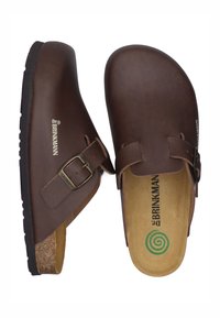 Braune Lederpantoletten mit runder Schuhspitze, verstellbarem Riemen mit einer Messingschnalle und einem Korkfußbett. Die Rückseite verfügt über eine strukturierte Gummisohle.