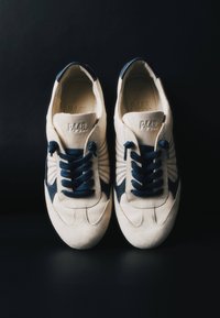 Paire de baskets blanches et bleu marine avec des lacets noirs placées côte à côte sur un fond sombre, vues de dessus.