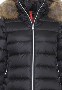 Giacca a vento nera con design a quadretti, chiusura frontale con zip e cappuccio foderato in pelliccia. Presenta un'etichetta interna rossa in contrasto.