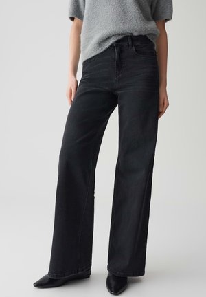 Jeans neri a gamba larga con vita alta e cinque tasche, realizzati in denim. Indossati con un maglione grigio soffice e scarpe nere a punta.
