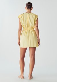 Geltonas trumpas suknelė su elastingu juosmeniu, trumpomis rankovėmis ir laisvu siluetu. Lygus paviršius su užsegimu gale ant kaklo.