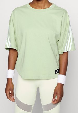 Personne portant un t-shirt Adidas vert clair avec des bandes blanches aux manches, des bracelets blancs et des leggings pâles avec des bandes grises.