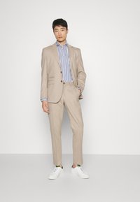 Costume beige ajusté avec une chemise rayée bleu clair et blanche. Comprend deux boutons, un pantalon droit et des baskets blanches. Design simple.