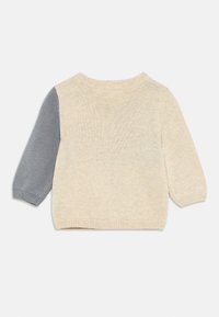 Ljusbeige tröja med en grå ärm. Mjuk stickad textur, rund halsringning och ribbade ärmslut och nederkant. Enkel, färgblockerad design.