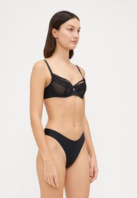 Zwart lingerieset met een doorschijnende mesh-beha met kantafwerking en bijpassende high-waisted onderbroek, met een gladde textuur en minimalistisch ontwerp.