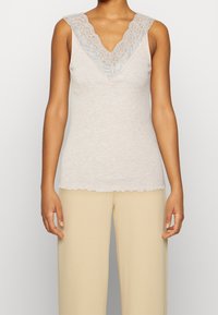 Débardeur beige clair avec un décolleté en V en dentelle. Tissu texturé avec un ourlet festonné. Sans manches, associé à un bas beige.