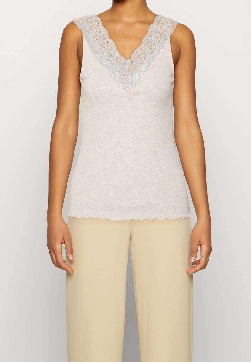 Débardeur beige clair avec un décolleté en V en dentelle. Tissu texturé avec un ourlet festonné. Sans manches, associé à un bas beige.