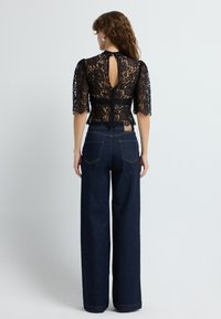 Sort blonderet top med korte puffærmer, der har en nøglehulslukning bagpå. Kombineret med højalvede mørke denim wide-leg bukser. Letvægts tekstur.