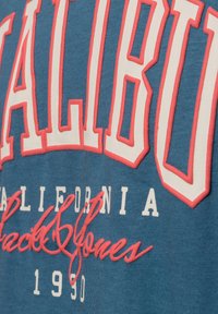 Sudadera azul con "MALIBU" en letras grandes blancas y rosas, con "California" y "1990" en texto más pequeño. Tejido suave y texturizado.