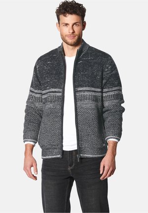 Men's zip-up cardigan in textured black and white knit. Features striped patterns and ribbed cuffs, paired with a white t-shirt underneath.