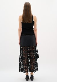 Black knit top with white trim, paired with a black layered skirt featuring intricate lace floral patterns. Model wearing block-heeled shoes.