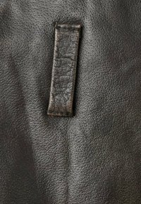 Primer plano de cuero negro mostrando una superficie texturizada con una correa rectangular, que presenta un aspecto ligeramente desgastado y sutiles patrones de grano.