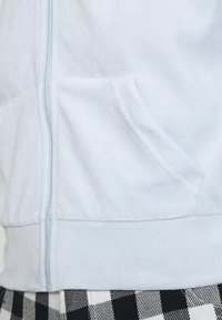 Felpa con zip di colore blu chiaro, caratterizzata da una texture morbida, tasca laterale e orlo a costine, abbinata a un motivo a scacchi in bianco e nero sotto.