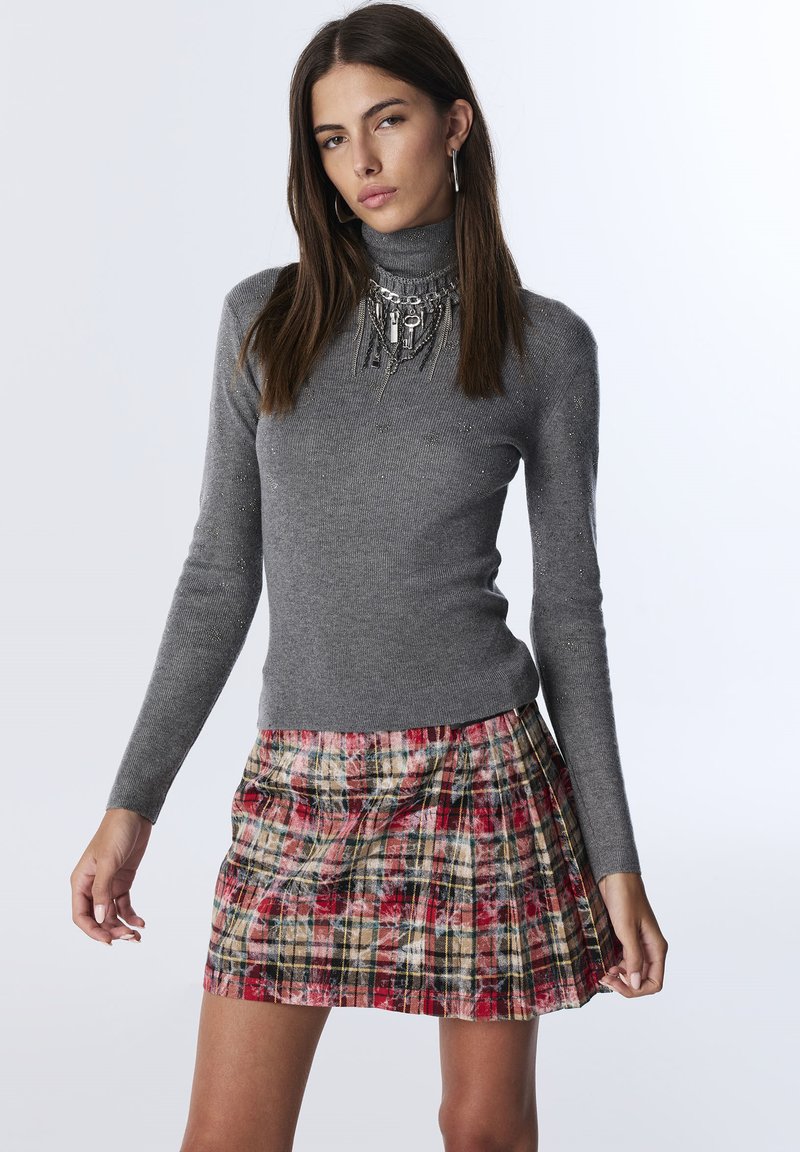 Szary sweter z golfem z metaliczną nicią, w połączeniu z plisowaną mini spódnicą w wielokolorowy kraciasty wzór w odcieniach czerwieni, kremu i czerni.