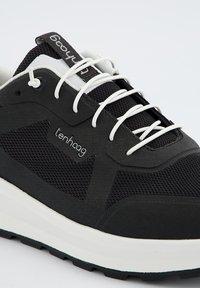 Chaussure de sport noire en mesh et caoutchouc, avec des lacets blancs et une semelle texturée. Le logo de la marque est affiché sur le côté.