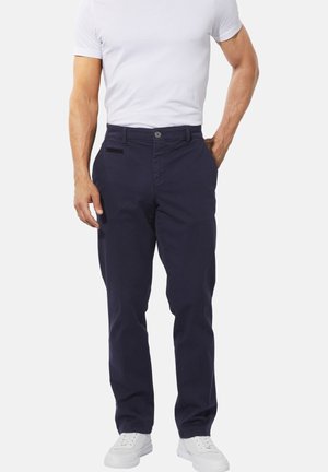 Navy blue chinos made of cotton. Features a button closure, front pockets, and a straight leg design. Worn with a white t-shirt and sneakers.