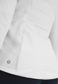 Veste de sport blanche en tissu texturé, avec un design matelassé, de subtiles perforations le long de la couture et un logo près de l'ourlet.