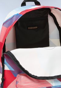 Mochila con un patrón geométrico colorido en rojo, azul y blanco. Cuenta con un bolsillo interior negro con cremallera y una etiqueta de logo. Tela texturizada.