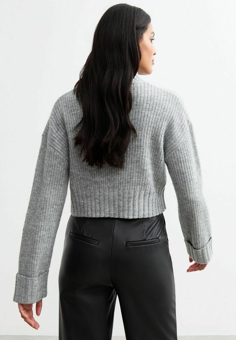 Maglione corto a coste grigio con spalle cadenti e polsini ampi, abbinato a pantaloni neri aderenti con tasche posteriori.