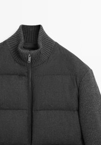 Dark gray padded jacket with ribbed high collar and knit textured sleeves, front zipper closure, shown from the upper chest to collar area.