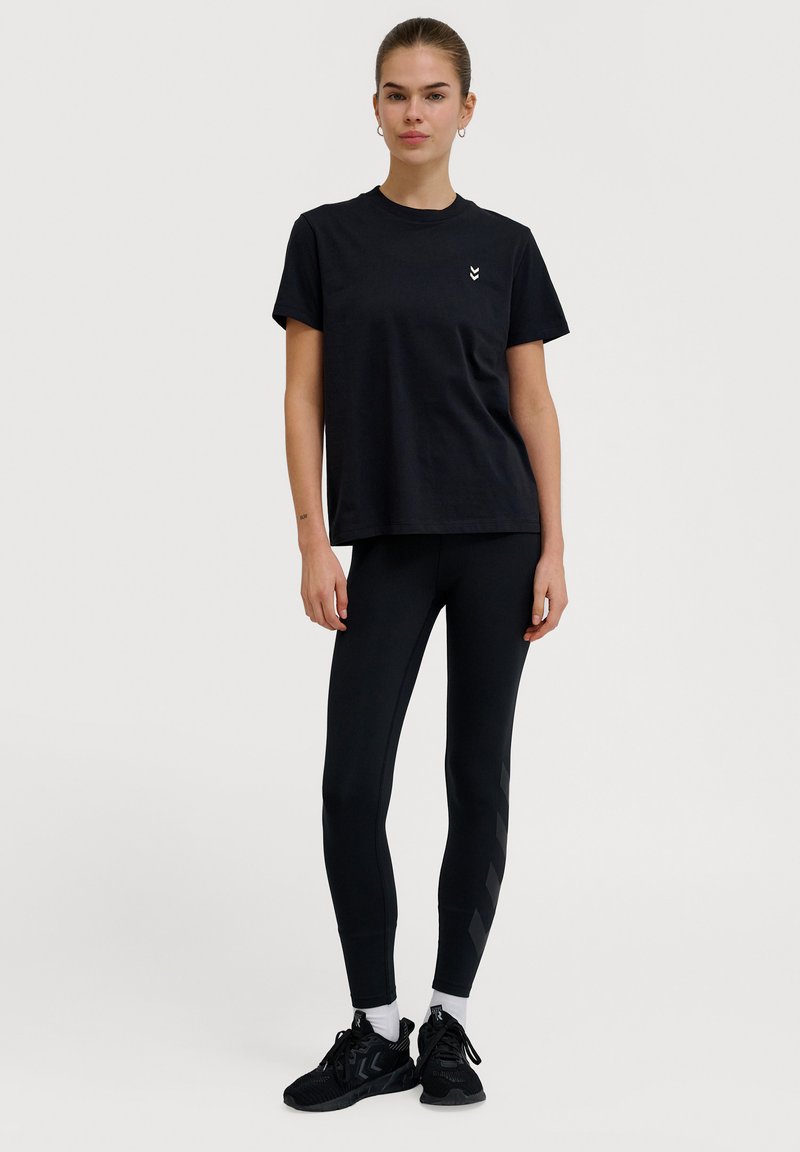 Sort bomulds t-shirt med korte ærmer og et subtilt logo; parret med sorte leggings med et diagonalt mønster og sorte sneakers.