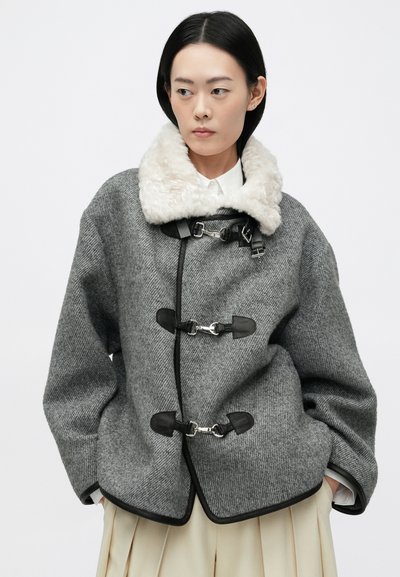 Siva jakna od vune s krznenim ovratnikom, s oznakama za zakopčavanje, crnim akcentima i opuštenim krojem. Glatka tekstura, dizajn zaobljenog hem.