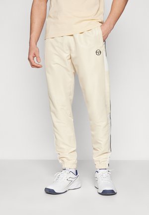 Pantalons de sport couleur crème avec des poignets élastiques, des rayures sur les côtés et un logo à l'avant. Fabriqués en tissu lisse et léger.